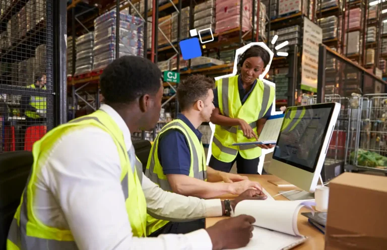 Une responsable sécurité anime un quart d’heure sécurité avec des collaborateurs en gilet fluorescent dans un entrepôt logistique, autour d’un ordinateur et de documents de prévention.