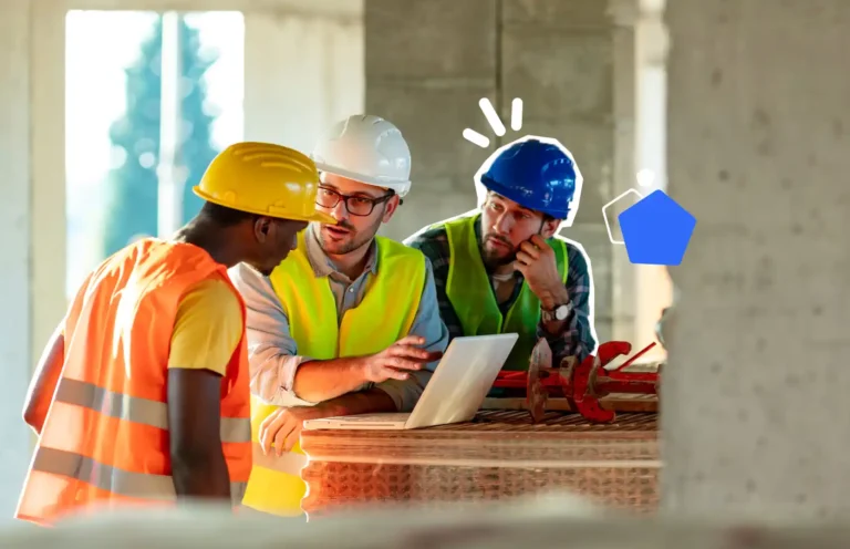 Trois professionnels du bâtiment en gilet de sécurité et casque discutent autour d’un ordinateur portable sur un chantier pour organiser la prévention des risques.