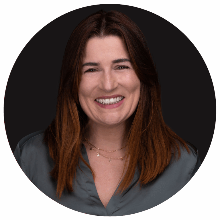 femme rousse qui souris sur fond noir, chelise verte et deux colliers autour du coup.